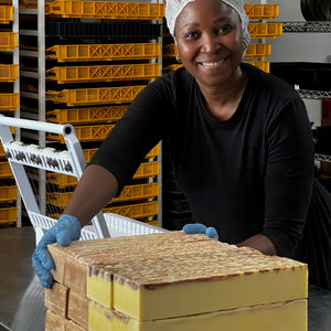 Zikhona Tefu  in a warehouse setting with stacked handmade soap blocks on a table